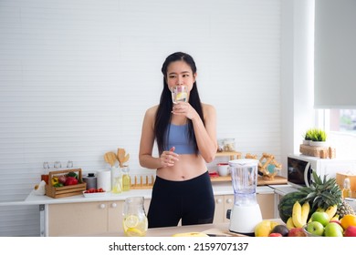 Fit And Healthy Young Asian Woman In Sportswear Preparing And Drinking Fresh Lemon Water For Healthy Lifestyle And Fitness In Modern Kitchen After Morning Workout And Exercise At Home