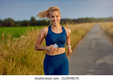 Fit healthy young woman enjoying a jog along a country road passing the camera with a happy smile full of vitality in an active lifestyle concept - Powered by Shutterstock