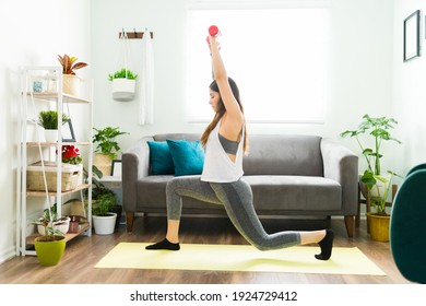 Fit Hispanic Woman Using Dumbells In Her Home Workout. Young Woman Doing Leg Plunges And Lifting Weights In Her Living Room Home