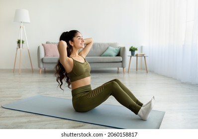 Fit Indian Woman Exercising On Yoga Mat, Strengthening Abs Muscles At Home, Full Length. Beautiful Eastern Female Keeping Fit And Healthy In Living Room. Domestic Sports During Covid Lockdown