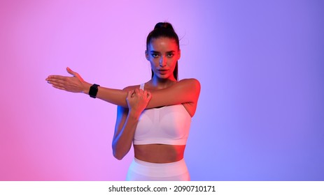Fit Lady In White Fitwear Stretching Arms Wearing Smart Fitness Watch Exercising Looking At Camera Standing On Pink And Blue Neon Background. Sport Motivation. Studio Shot, Panorama - Powered by Shutterstock