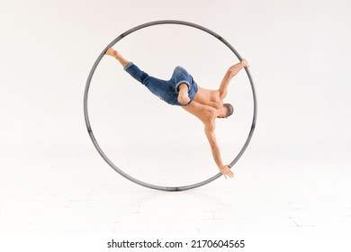 Fit male acrobat performing a one leg handspring on a cyr wheel while in spinning motion over a white background with copyspace