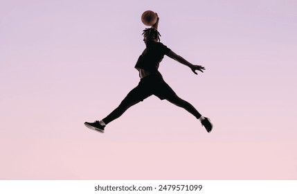 Fit male basketball player with dreadlocks jumps to dunk the ball during a game. His silhouette stands out against a pink background, showcasing his athleticism and scoring skills. - Powered by Shutterstock