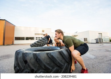 Fit male and female athletes doing tire-flip exercise outdoors - Powered by Shutterstock