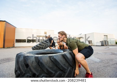 Fit male and female athletes doing tire-flip exercise outdoors