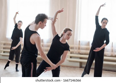 Fit male instructor of dancing course standing by one of girls in activewear while helping her with exercise during training - Powered by Shutterstock