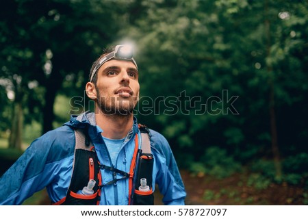 Fit male jogger with a headlamp rests during training for cross country trail race in nature park.