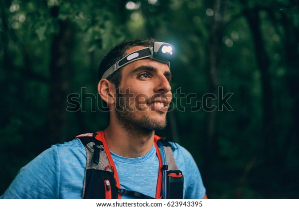Fit male jogger with a\
headlamp rests during training for cross country trail race in\
nature park.