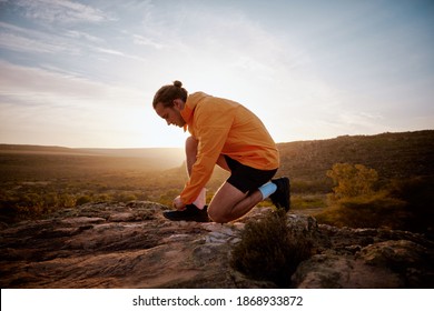 Fit male jogger tying shoelace preparing for cross country mountain trail in nature - morning run in the mountains