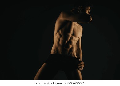 Fit male revealing well-defined abs and muscular torso, emphasizing physical fitness and strength under dramatic lighting in a dark studio background. - Powered by Shutterstock