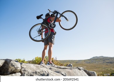 Fit man carrying his bike on rocky terrain on a sunny day - Powered by Shutterstock