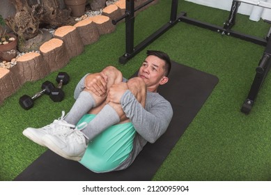 A fit man does lying knee tucks on a black mat. Stretching and warming up before a workout at the home gym.