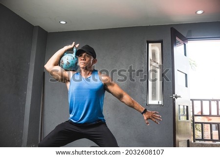 A fit man does single arm shoulder thrusters with a kettlebell. Intense HIIT or upper body workout at the gym.