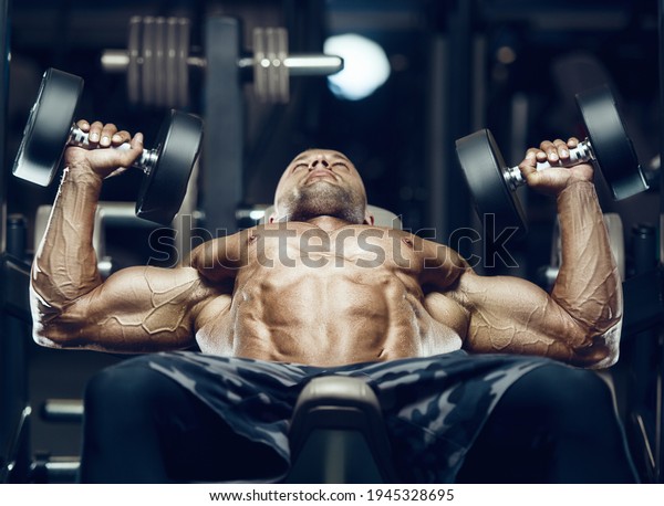 fit man\
doing bench press with dambells. Training pectoral muscles at gym.\
Pumping up chest exercise. Close up muscles at workout.\
Bodybuilding, fitness and health care\
concept.