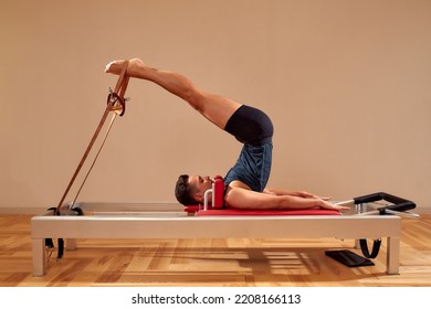 Fit man doing a lunge stretch yoga pilates exercise to strengthen and tone his muscles using a reformer in gym. Health and fitness concept - Powered by Shutterstock