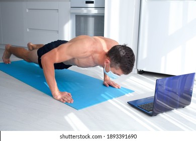 Fit Man Doing Squeeze-up And Watching Online Lessons On Laptop While Exercising In The Kitchen. Man Wearing Medical Mask Exercise During The COVID-19