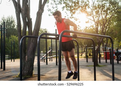 Fit man doing triceps dips on parallel bars at park exercising outdoors