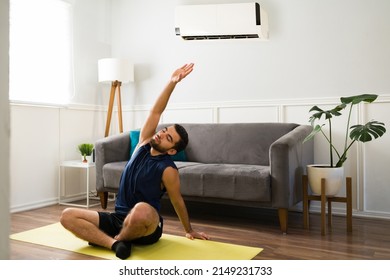 Fit Man Doing Yoga At Home During Summer. Young Man Exercising In The Hot Weather With The Cool Air Conditioner 