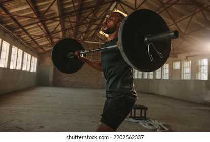 Fit man exercising barbell in old warehouse. Strong male athlete lifting weights. - Powered by Shutterstock