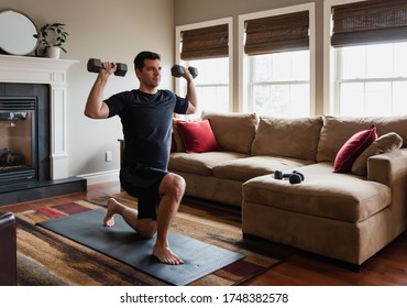 Fit man exercising at home with hand weights in his living room.