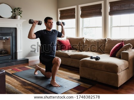 Fit man exercising at home with hand weights in his living room.