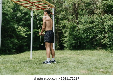 Fit man exercising in nature using monkey bars and resistance band in an outdoor park, showcasing a healthy lifestyle and physical fitness. - Powered by Shutterstock