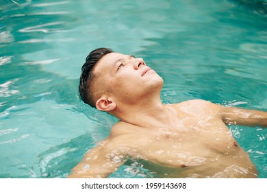 Fit Man Floating On Back In Swimming Pool And Looking At Sky