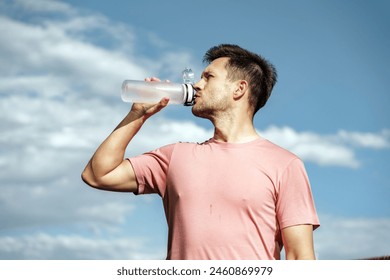 A fit man hydrates by drinking water from a bottle after a workout, under a clear blue sky.

 - Powered by Shutterstock