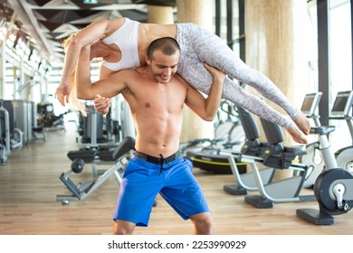 Fit man lifting sporty woman up at gym.