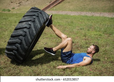 Fit man performing leg workout with tier during obstacle course in boot camp - Powered by Shutterstock