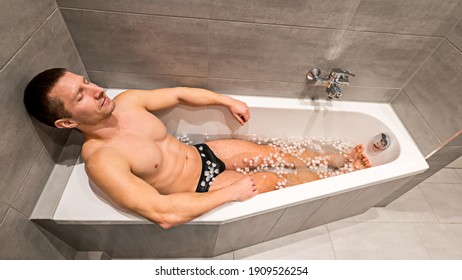 Fit man sitting in a bathtub filled with cold water and ice cubes for recovery and health purposes