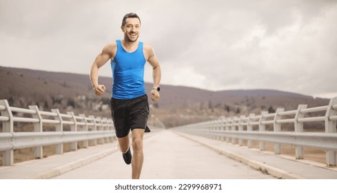 Fit man in sportswear running across a bridge on a cloudy day - Powered by Shutterstock