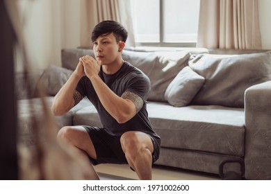 Fit Man In Sportwear Doing Squat Exercise At Home. Young Asian Man Doing Workout At Home. Home Exercise In Quarantine.