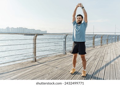 Fit man stretching arms upwards on a seaside boardwalk with city and bridge view. - Powered by Shutterstock