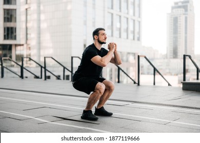 Fit Man Training Air Squat Exercise. Fit Male Exercising Crossfit Outside. Young Handsome Caucasian Male Fitness Model And Instructor Outdoors. Black Sportswear. Sport In Big City Concept.