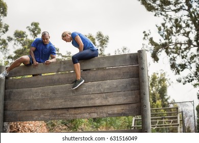 Fit Man And Woman Climbing Over Wooden Wall During Obstacle Course In Boot Camp