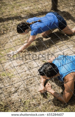 Fit man and woman crawling under the net during obstacle course in boot camp