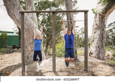 Fit man and woman performing pull-ups on bar during obstacle course in boot camp - Powered by Shutterstock