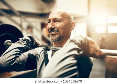 Fit Mature Man In Sportswear Smiling While Lifting Heavy Weights During A Workout Session In A Gym