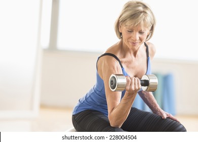 Fit mature woman lifting dumbbell while sitting at home