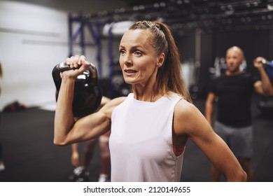 Fit mature woman in sportswear lifting a dumbbell during a strength training session at the gym - Shutterstock ID 2120149655