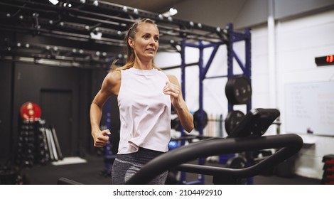 Fit mature woman in sportswear smiling while working out on a running machine at the gym - Shutterstock ID 2104492910