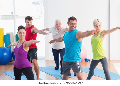 Fit Men And Women Doing Warrior Pose In Yoga Class