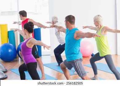 Fit Men And Women Doing Warrior Pose In Yoga Class