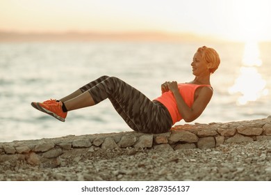 Fit middle age woman doing sit-up exercises during hard training near the sea beach. - Powered by Shutterstock