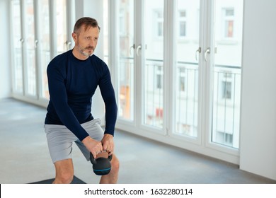 Fit middle-aged man lifting a kettle weight in an airy spacious urban gym in a health and fitness concept