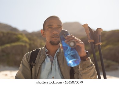 A fit, mixed race male athlete, enjoying his time on a trip to the mountains, hiking with sticks, drinking water beach, resting on the beach by the sea. Active lifestyle Nordic walking. - Powered by Shutterstock