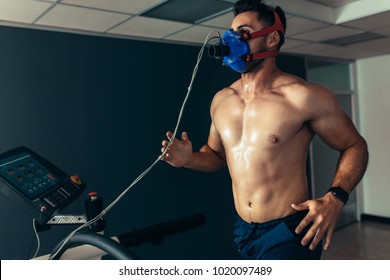 Fit And Muscular Athlete With Mask Running On Treadmill For Monitoring His Performance. Sportsman In Sports Science Lab Measuring His Performance.