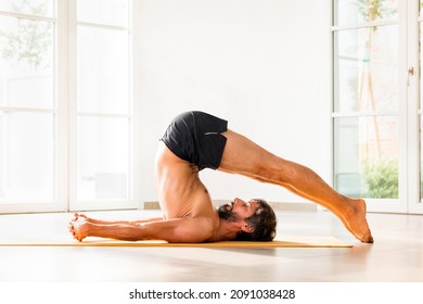 Fit Muscular Man Performing A Halasana Yoga Pose In A High Key Gym In A Low Angle Floor Level Side View In A Health And Fitness Concept