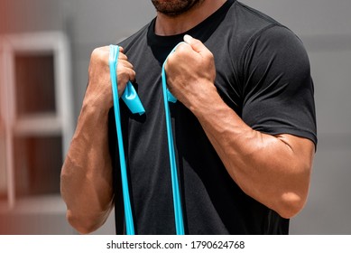 Fit Muscular Sports Man Doing Bicep Curl Exercise With Resistance Band Outdoors At Home In Sunlight